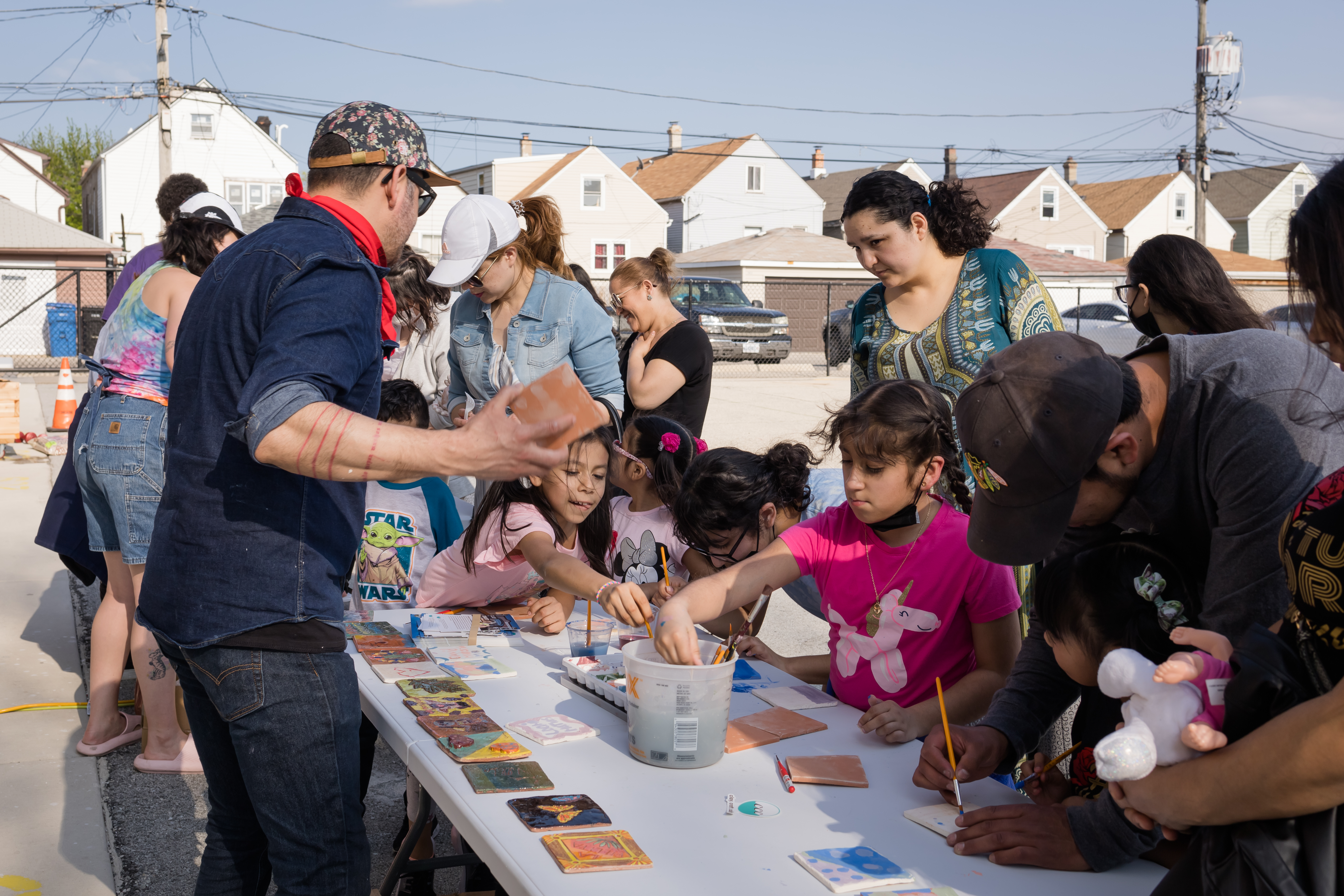 a group of young people paint clay tiles with their families